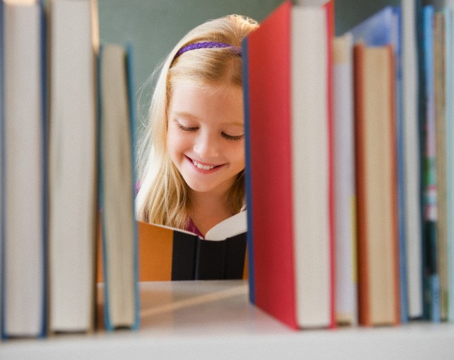 USA, New Jersey, Jersey City, View across the shelf showing girl (8-9) reading book