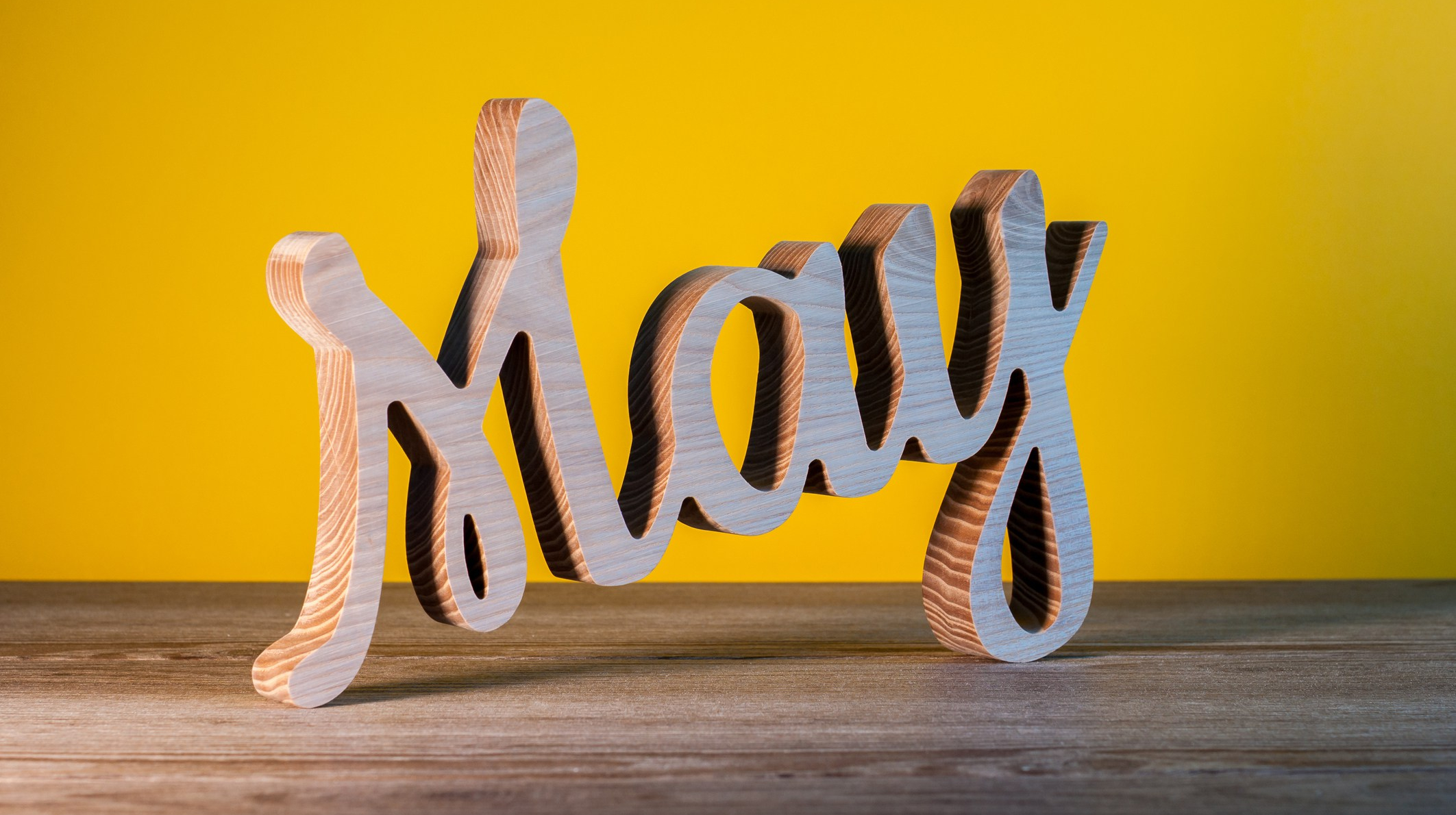 May -wooden carved name of spring month. Calendar on business office table, workplace at yellow background. Spring time